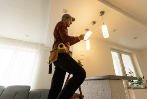 a-man-on-a-step-ladder-wearing-a-tool-belt-and-installing-a-light-fixture